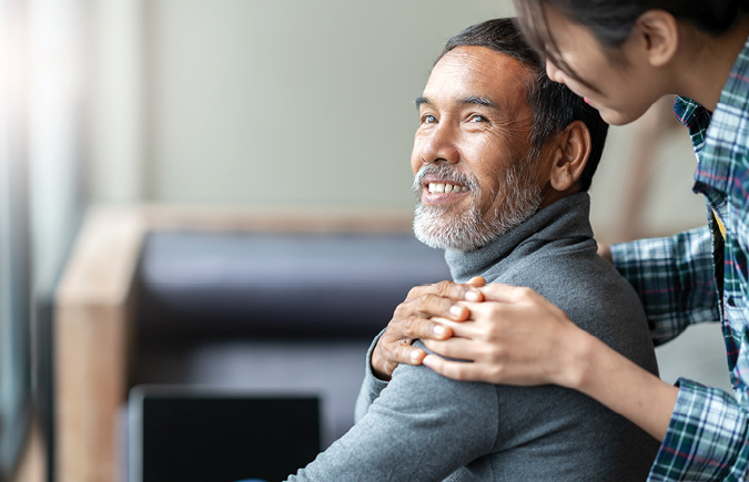 A retired man smiles and holds his daughter's hand at an assisted living facility.