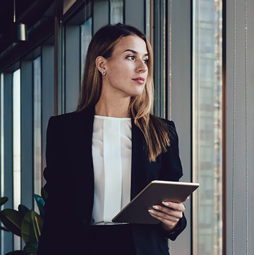 Young professional woman holding tablet device, looking out window